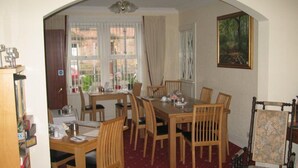 A dining area with a wooden table and chairs, a chandelier, and a painting on the wall. - Mardon Guest House (Inverness)