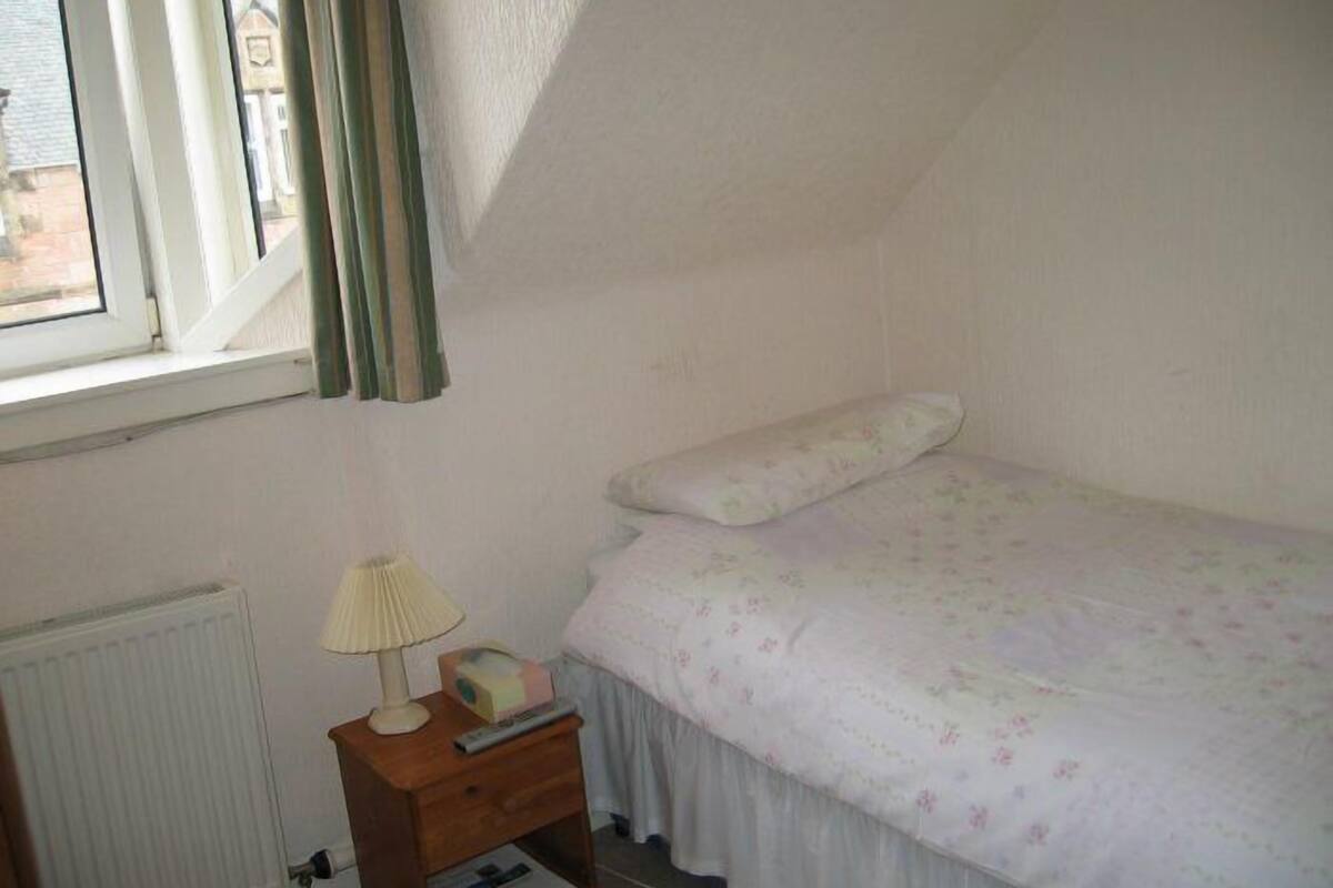 A bedroom with a single bed, a nightstand with a lamp, and a window with curtains.