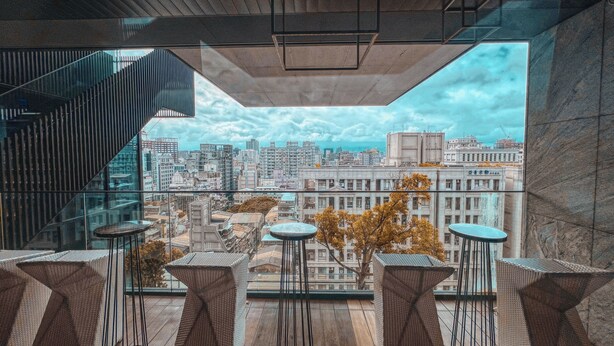A modern interior with a city view, featuring a staircase, multiple tables, and a geometric ceiling design. - Aloft Taipei Zhongshan (Taipei)