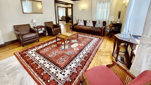 Un salón con un sofá de cuero marrón, un sillón de cuero marrón, una mesa de centro de madera y una alfombra estampada.