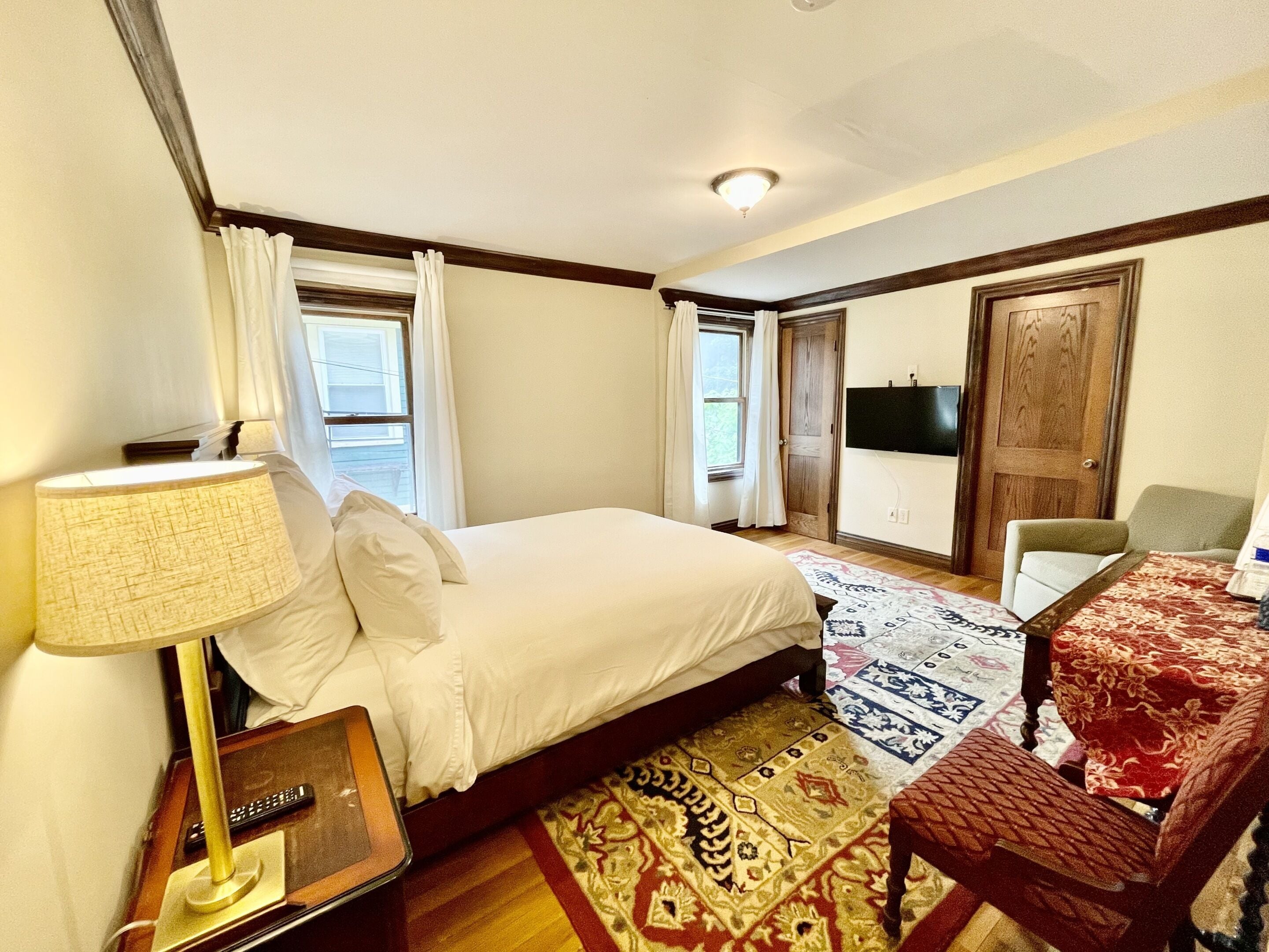 A hotel room with a bed, a desk with a lamp, a chair, a TV, and a door.