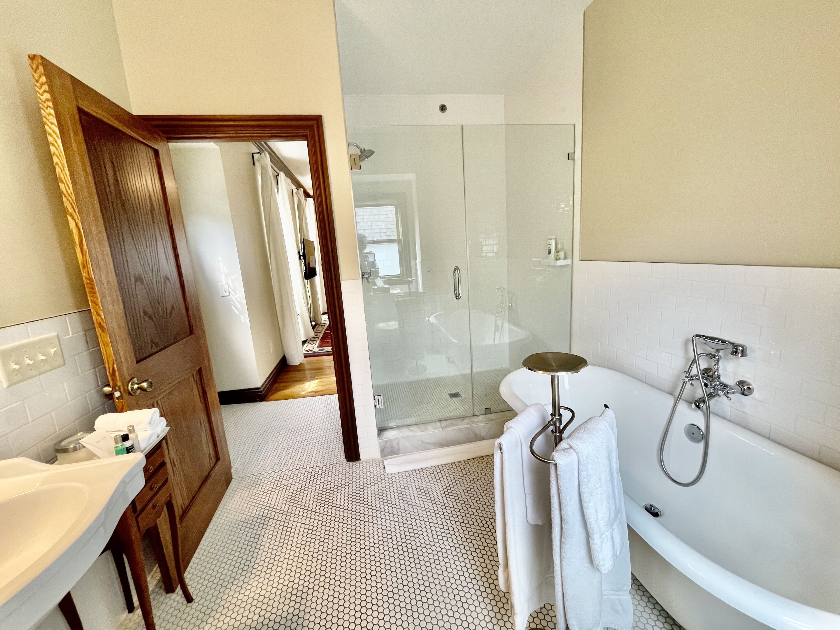 A bathroom with a glass-enclosed shower, a white bathtub, and a wooden door.