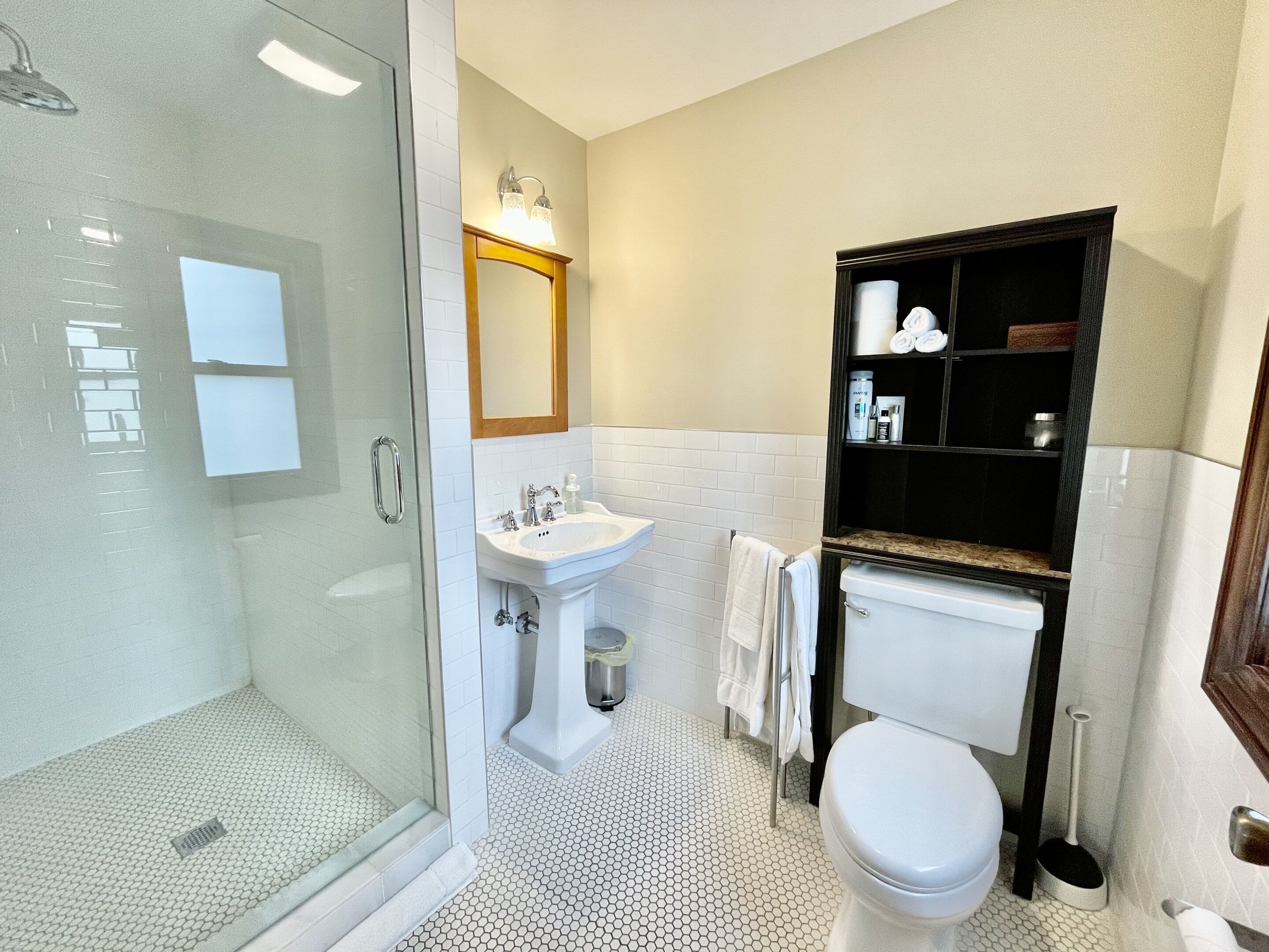 Ein Badezimmer mit Duschkabine, Standwaschbecken, Toilette und einem Waschtisch mit Regalen.