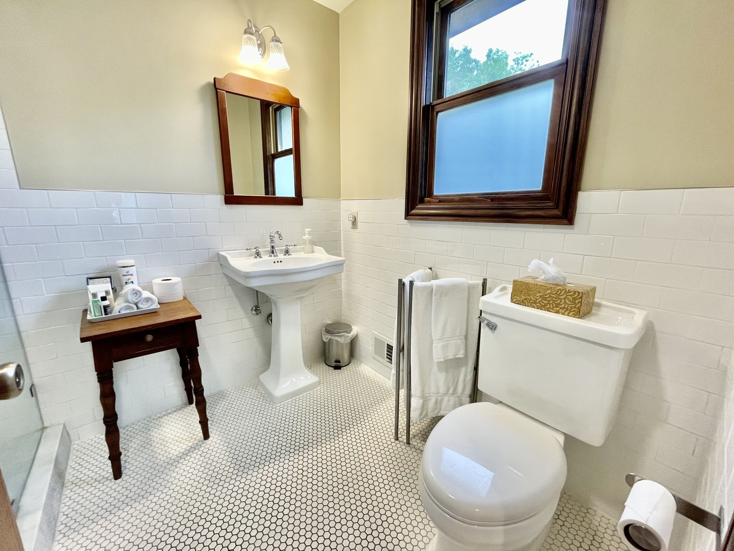 A bathroom with a white sink, toilet, and a small table with toiletries.