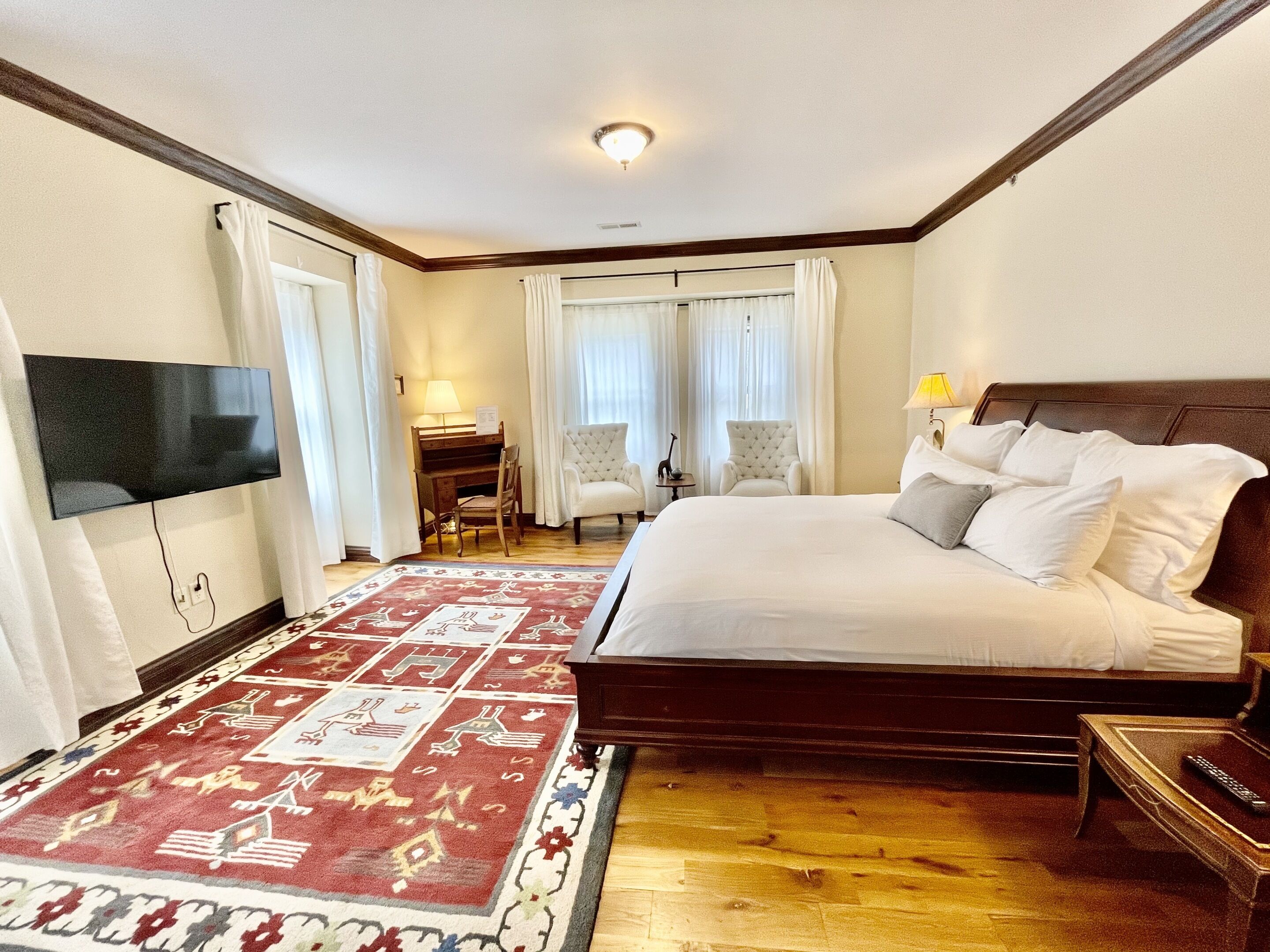 Quarto de hotel com uma cama grande, uma mesa com cadeira, uma televisão na parede e um tapete estampado.