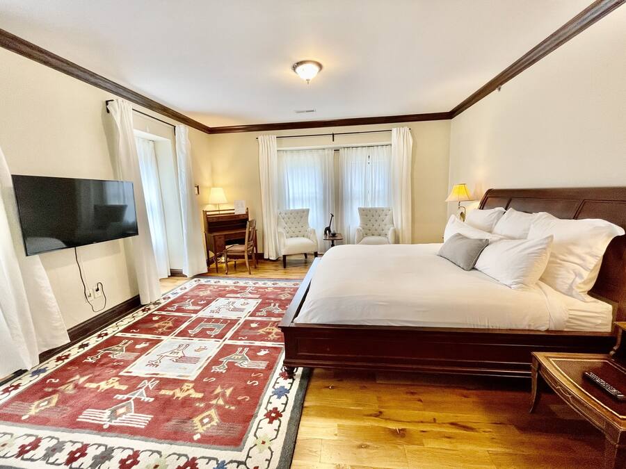 Quarto de hotel com uma cama grande, uma mesa com cadeira, uma televisão na parede e um tapete estampado.