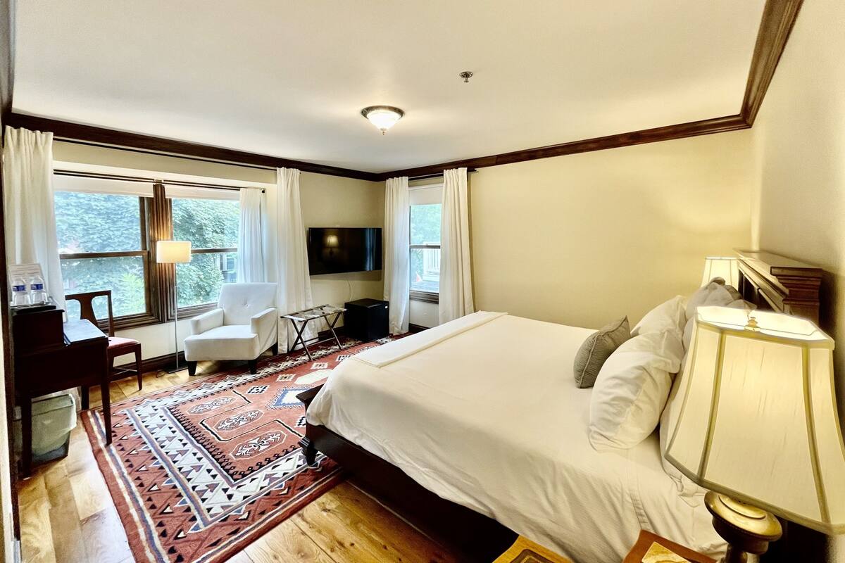 Ein Hotelzimmer mit einem großen Bett, einem Schreibtisch mit Stuhl, einem Fernseher und einem Fenster mit Vorhängen.