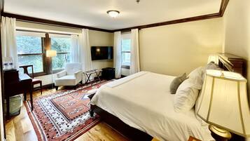 Una habitación de hotel con una cama grande, un escritorio con silla, un televisor y una ventana con cortinas.