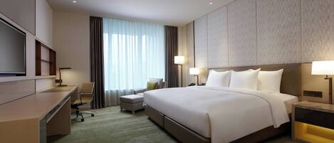 A hotel room with a large bed, a desk, a chair, a TV, and a lamp.