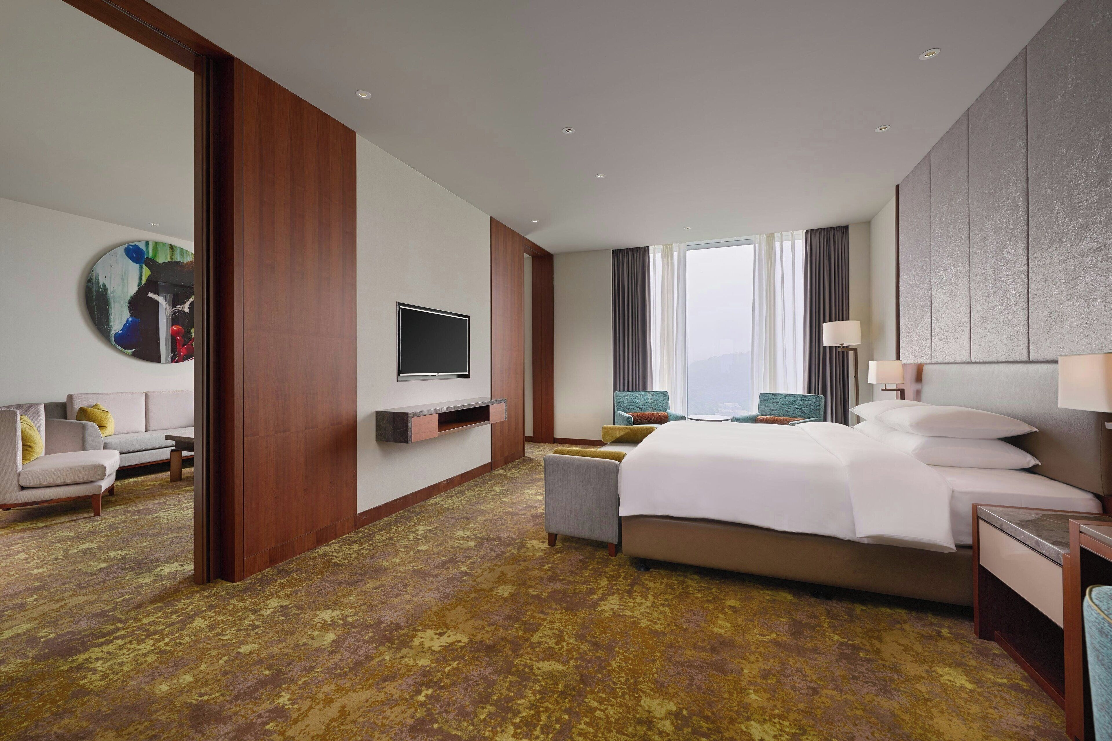 Una habitación de hotel con cama, televisor, sofá y un ventanal grande.