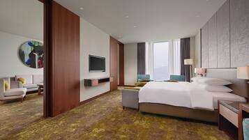 Una habitación de hotel con cama, televisor, sofá y un ventanal grande.