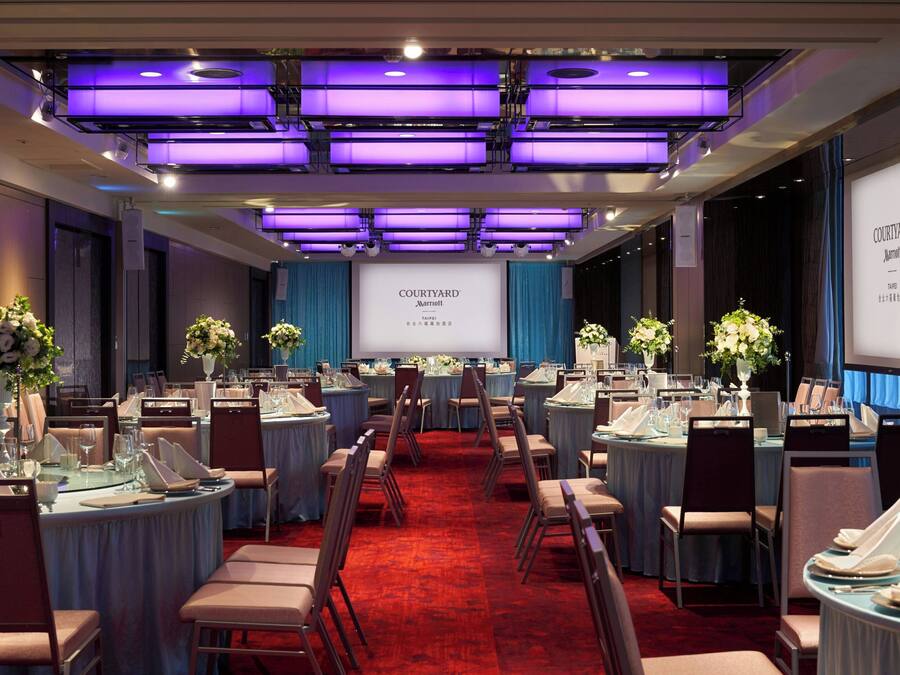 A conference room with round tables, chairs, and a large screen displaying 'COURTYARD Marriott'.