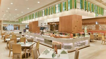 Uma ampla sala de jantar com várias mesas e cadeiras, um balcão de buffet com diversos alimentos, e teto alto com iluminação embutida.
