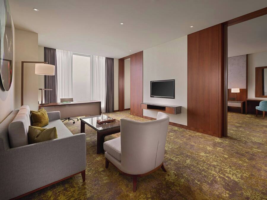Een hotelkamer met een bank, fauteuil, salontafel, televisie en een grote spiegel.