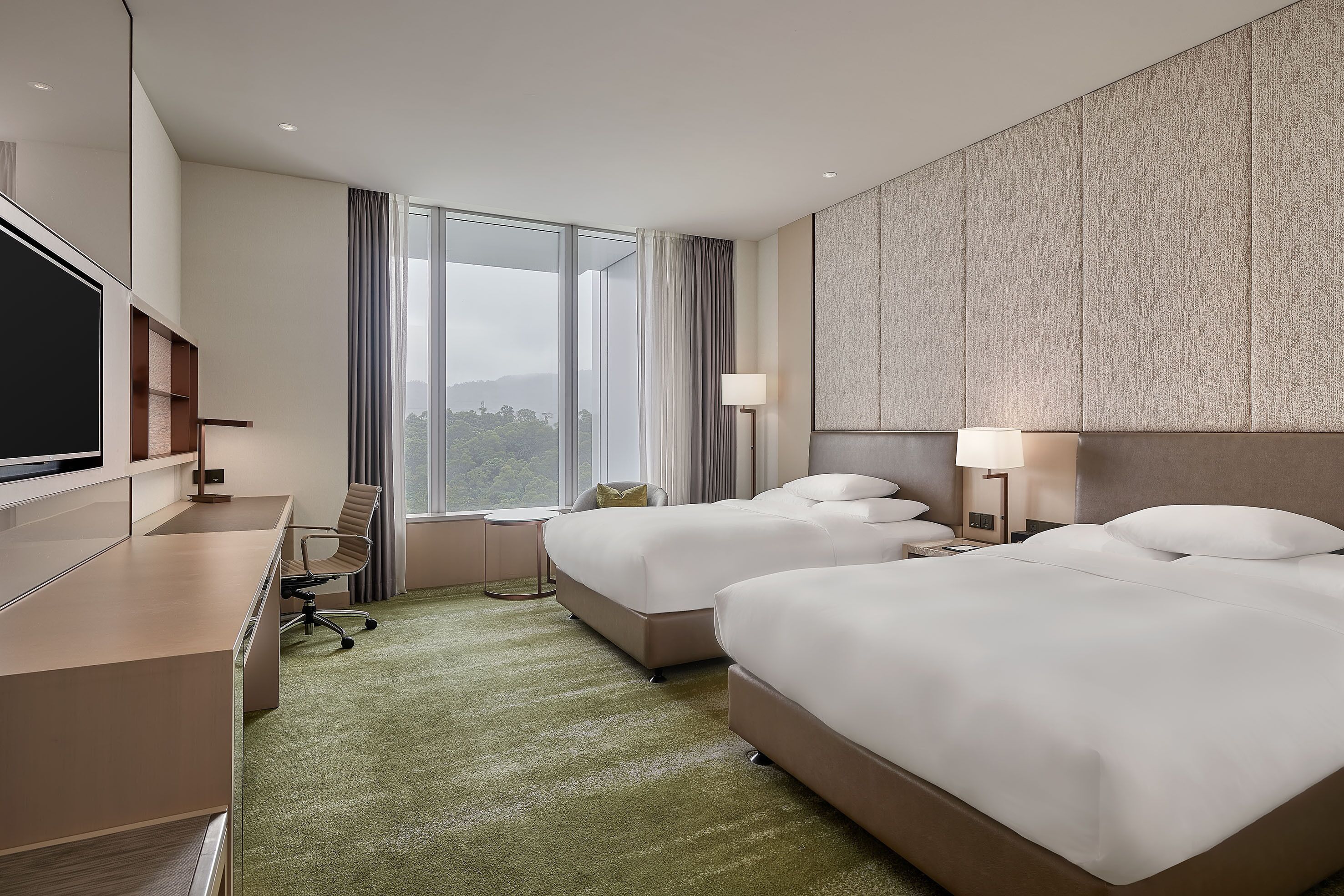 A modern hotel room with two beds, a desk, and a large window offering a view of the outdoors.