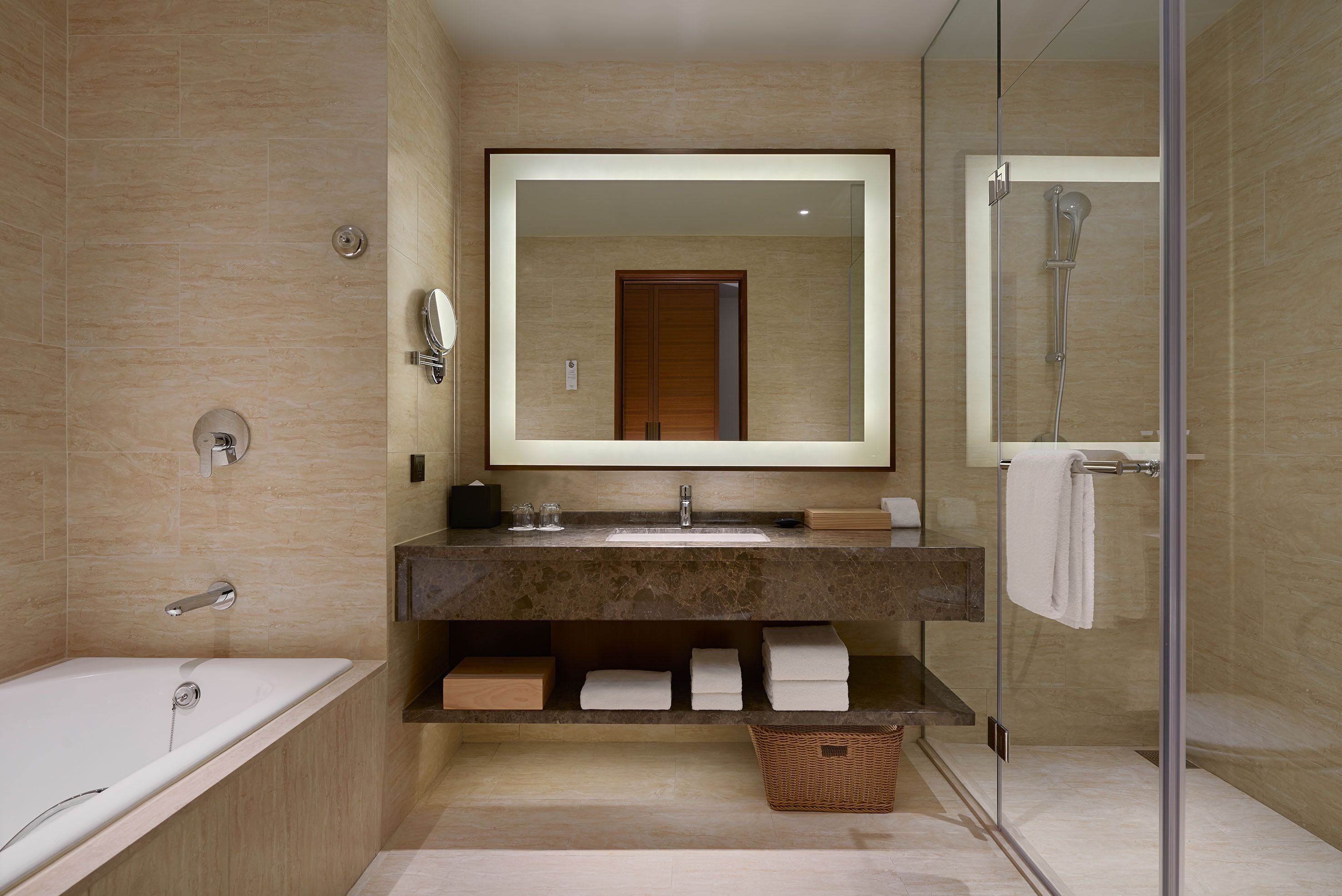 A modern bathroom with a bathtub, a large mirror, a shower, and a vanity with a sink and towel storage.