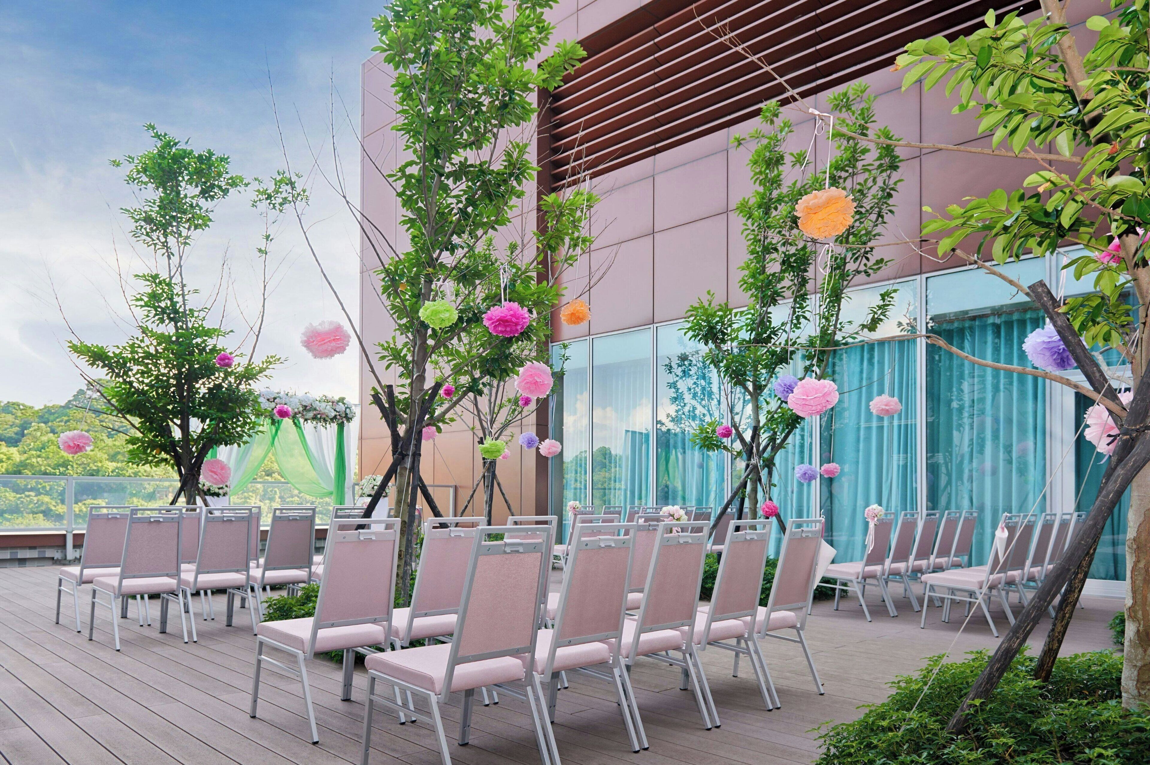 An outdoor seating area with chairs arranged in rows, surrounded by trees and decorative elements.