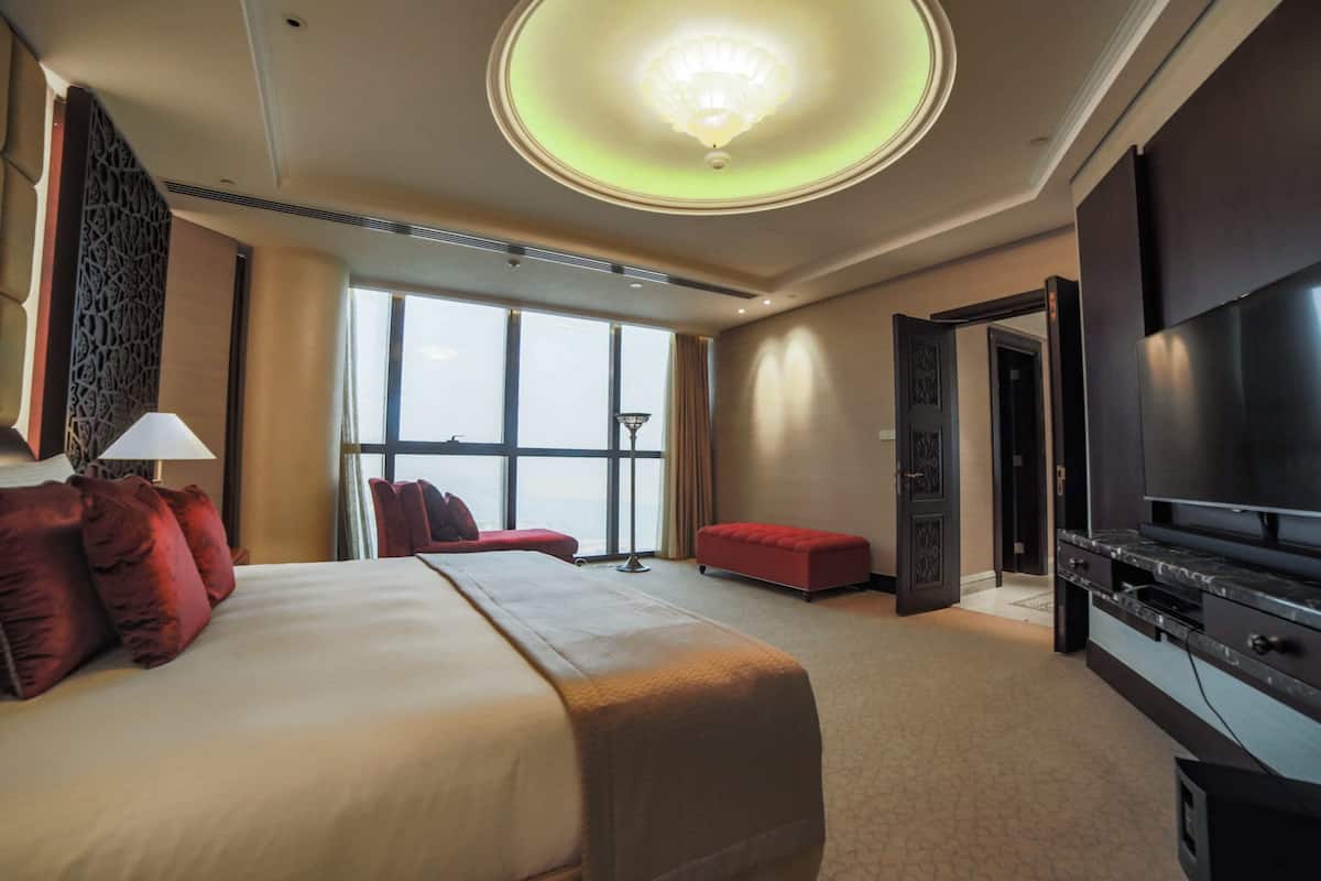 A hotel room with a large bed, a TV, and a view of the city through large windows.
