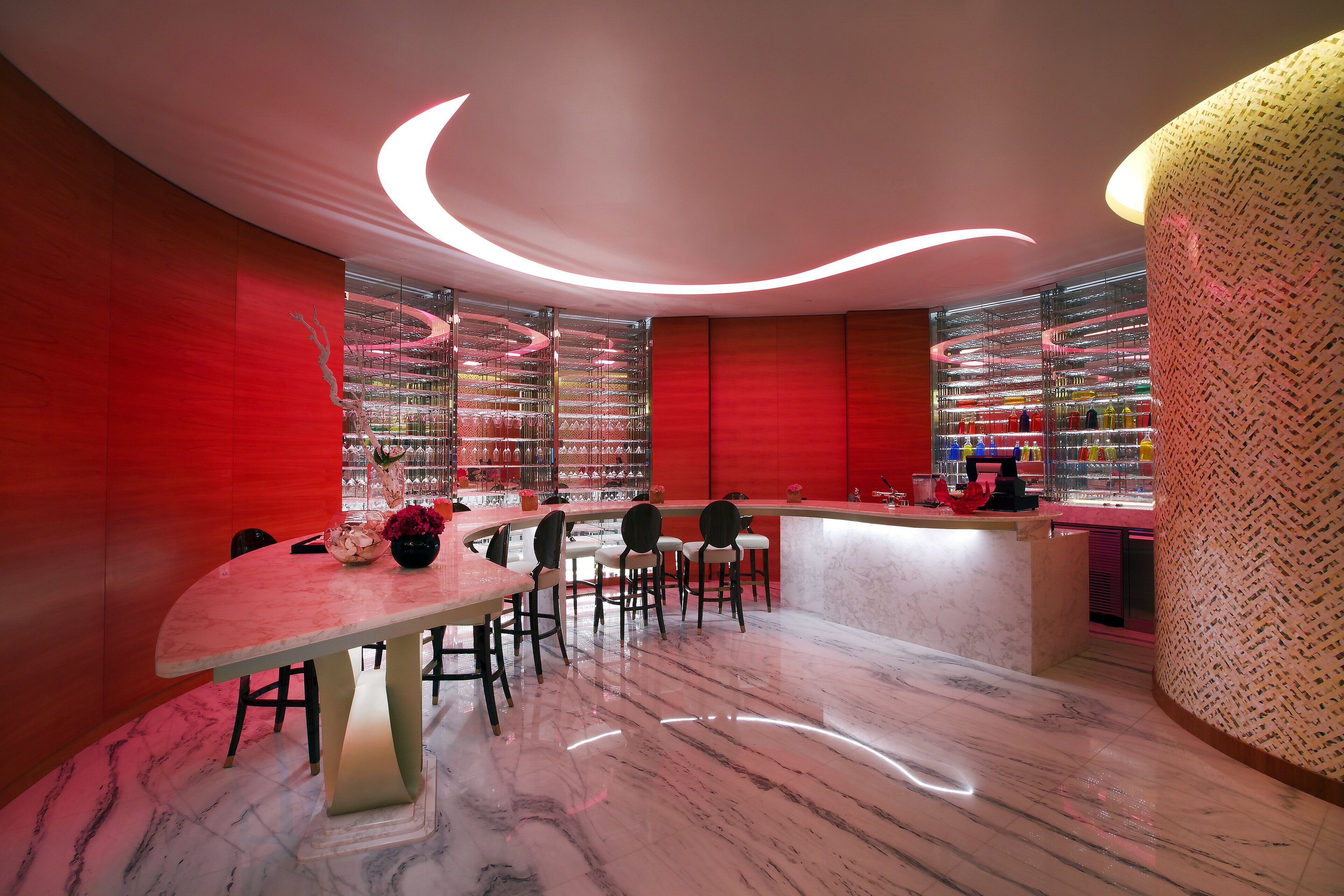 A modern interior with a curved dining table, bar area, and a red accent wall.