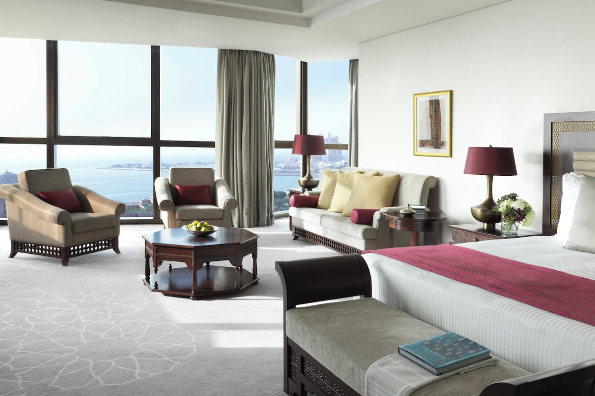 A hotel room with a large window, a sofa, a chair, a bed, and a small table.