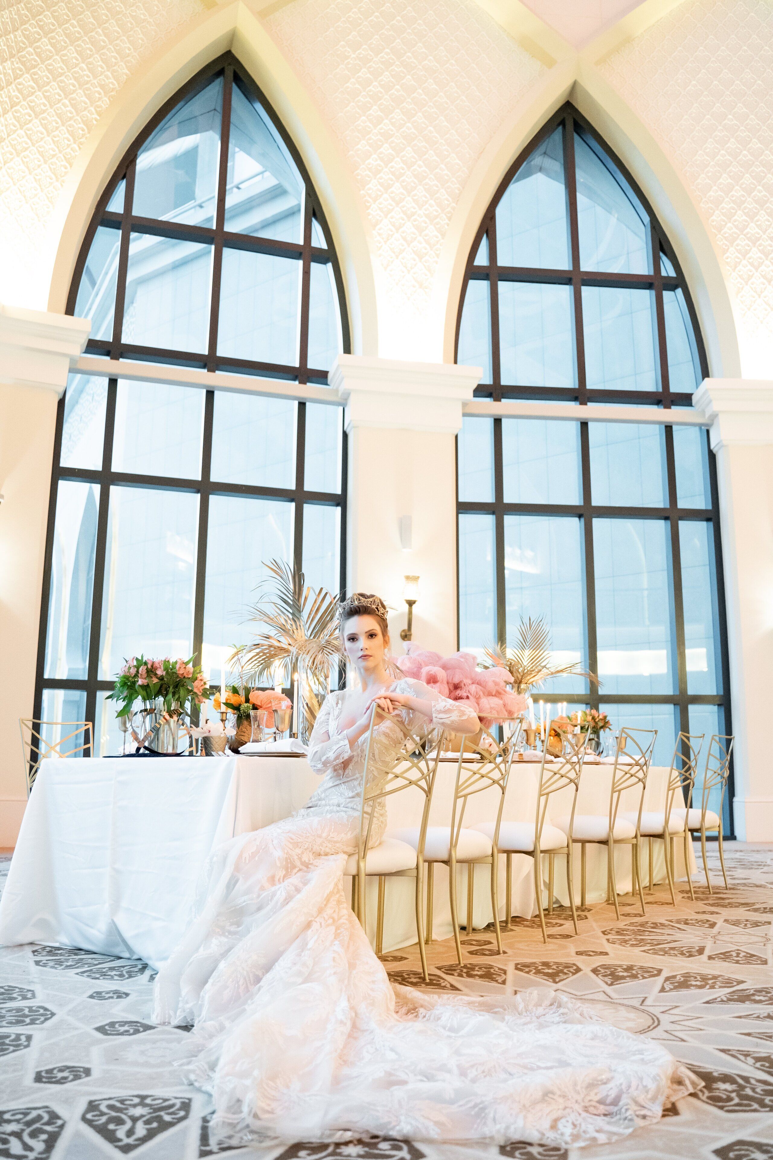 A wedding venue with a high arched window, a table set for a wedding, and a bride in a white dress.
