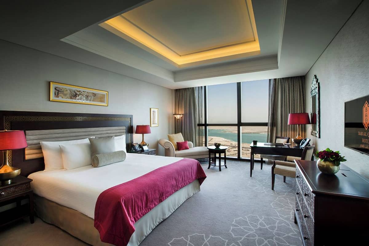 A hotel room with a large bed, a desk, a chair, and a view of the beach.