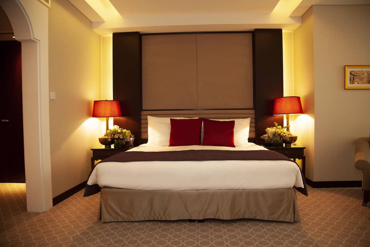 A hotel room with a large bed, two bedside tables with lamps, a chair, and a painting on the wall.