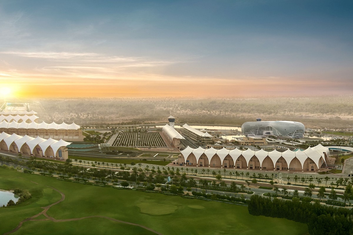 An aerial view of a modern architectural complex with a large stadium, a water body, and green spaces.