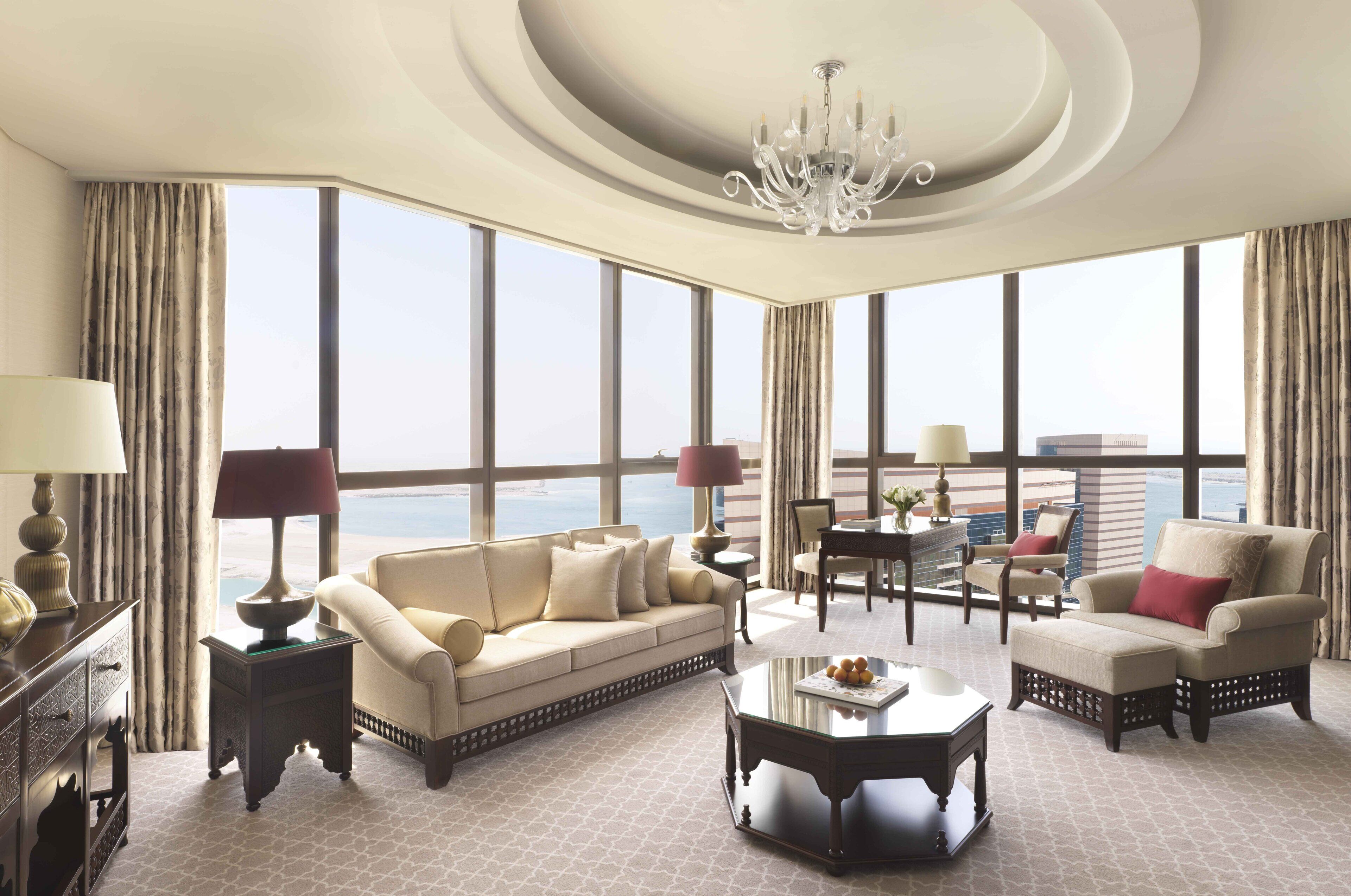 A spacious living room with a large window, a chandelier, and a view of the city.
