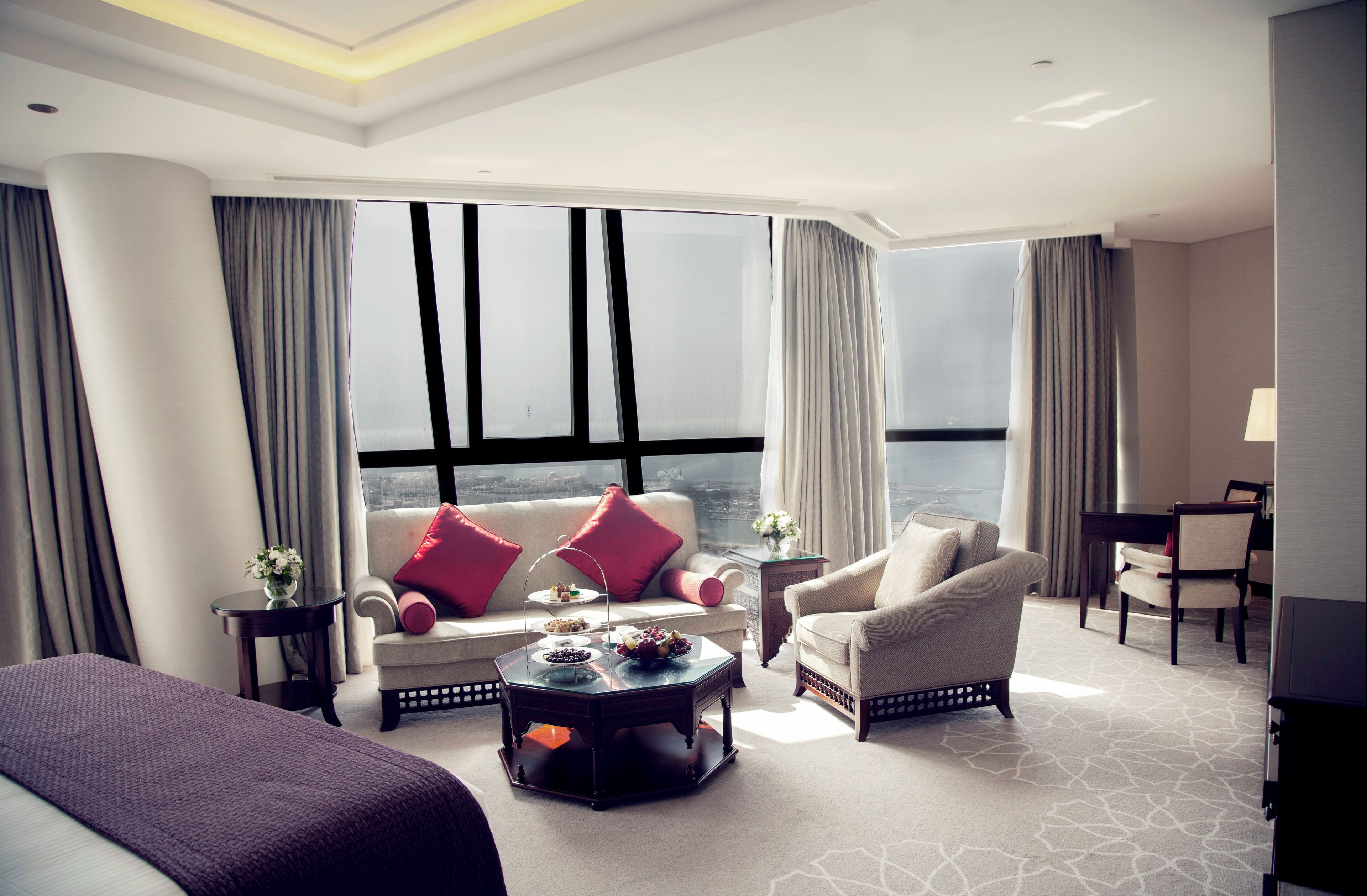 A modern hotel room with a large window, a sofa, a chair, a coffee table, and a bed.