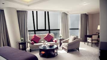 Una habitación de hotel moderna con un ventanal grande, un sofá, una silla, una mesita de centro y una cama.