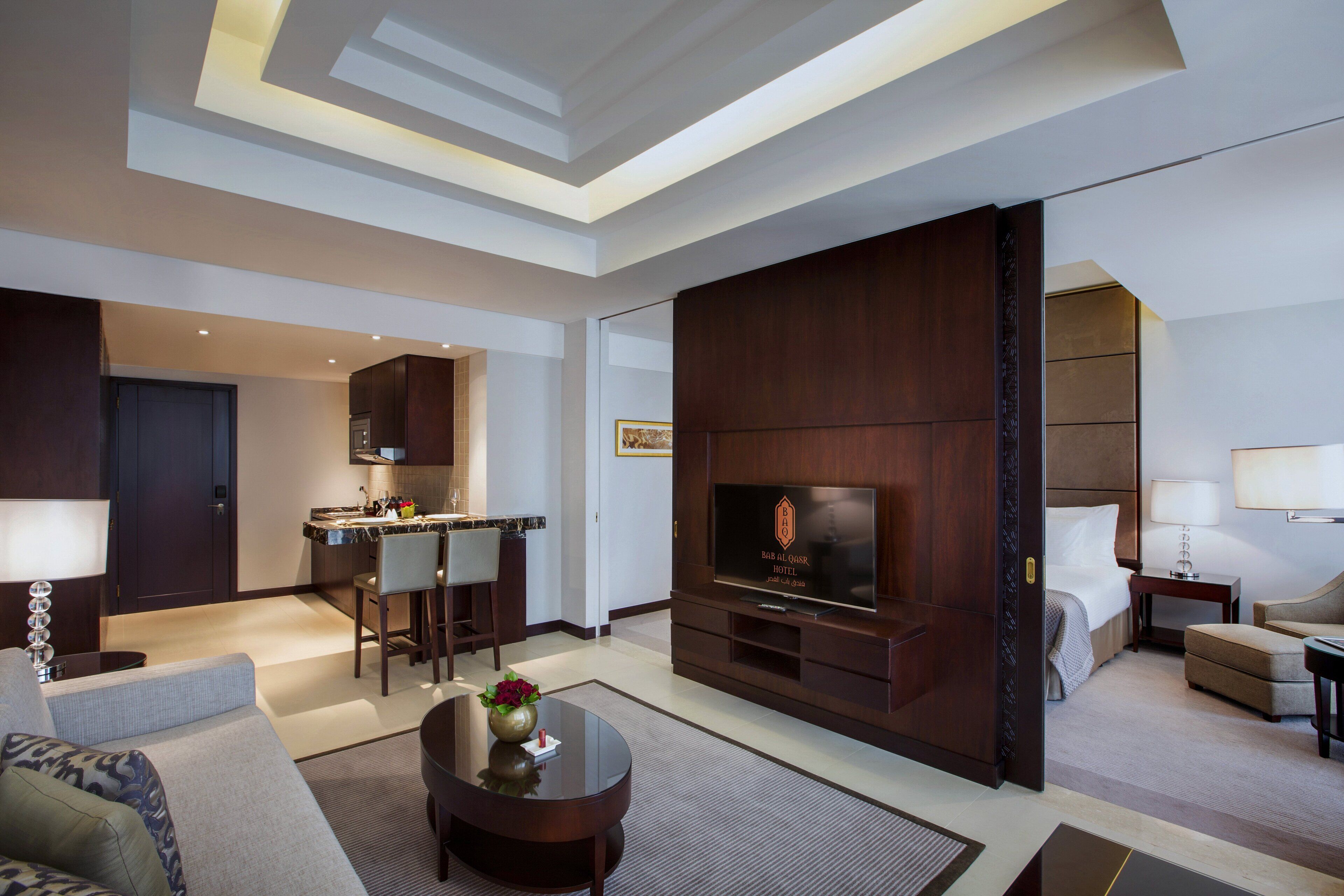 A modern hotel room with a living area, a dining area, and a TV.