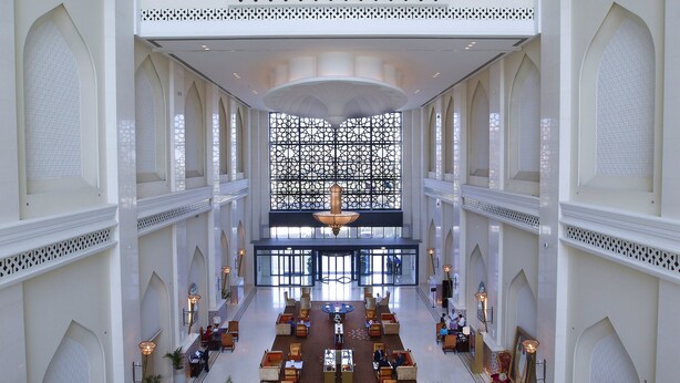 Un'ampia hall con soffitti alti, dettagli architettonici decorati e palme.