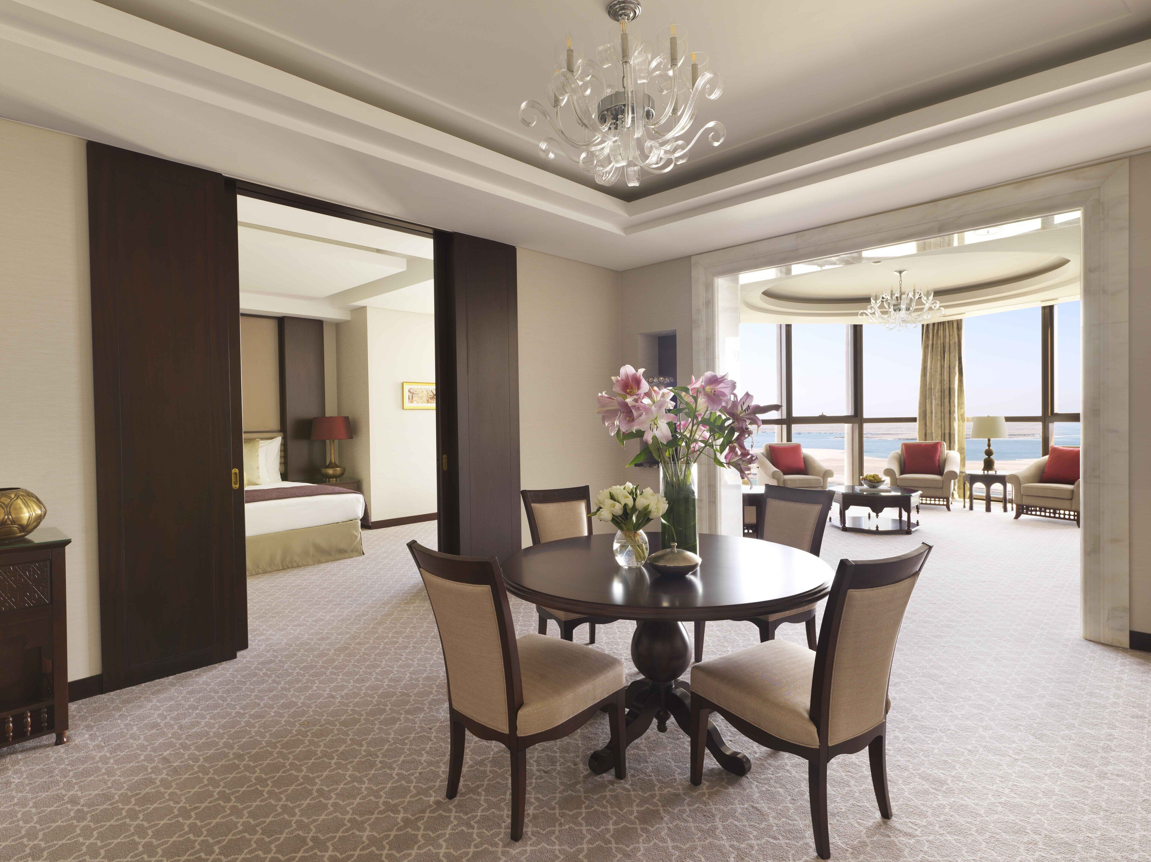A hotel room with a dining area, a large window with a view, and a chandelier.