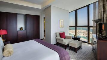 Ein Hotelzimmer mit einem großen Bett, einer Sitzecke mit Blick auf den Strand und einer Minibar.