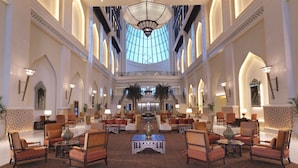 Een ruime lobby met hoge plafonds, weelderige kroonluchters en een centrale trap.