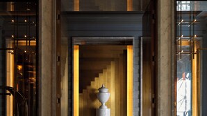 Un vestíbulo de mármol con una columna central, una escalera y una puerta de cristal que da a vistas de un edificio.
