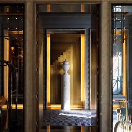 A marble lobby with a central column, a staircase, and a glass door leading to a view of a building.