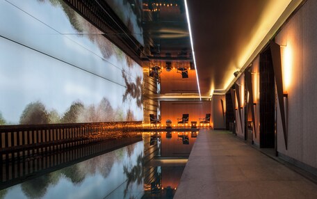 A modern hotel corridor with a reflective pool, seating area, and warm lighting.