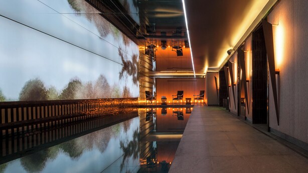 Pasillo moderno de hotel con piscina reflectante, zona de estar e iluminación cálida.