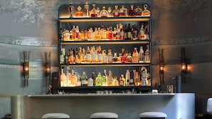 Un espace bar doté de plusieurs étagères remplies de bouteilles d’alcool, de tabourets de bar et d’une surface réfléchissante.