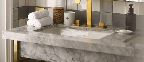 A bathroom with a marble sink, gold fixtures, and a mirror.