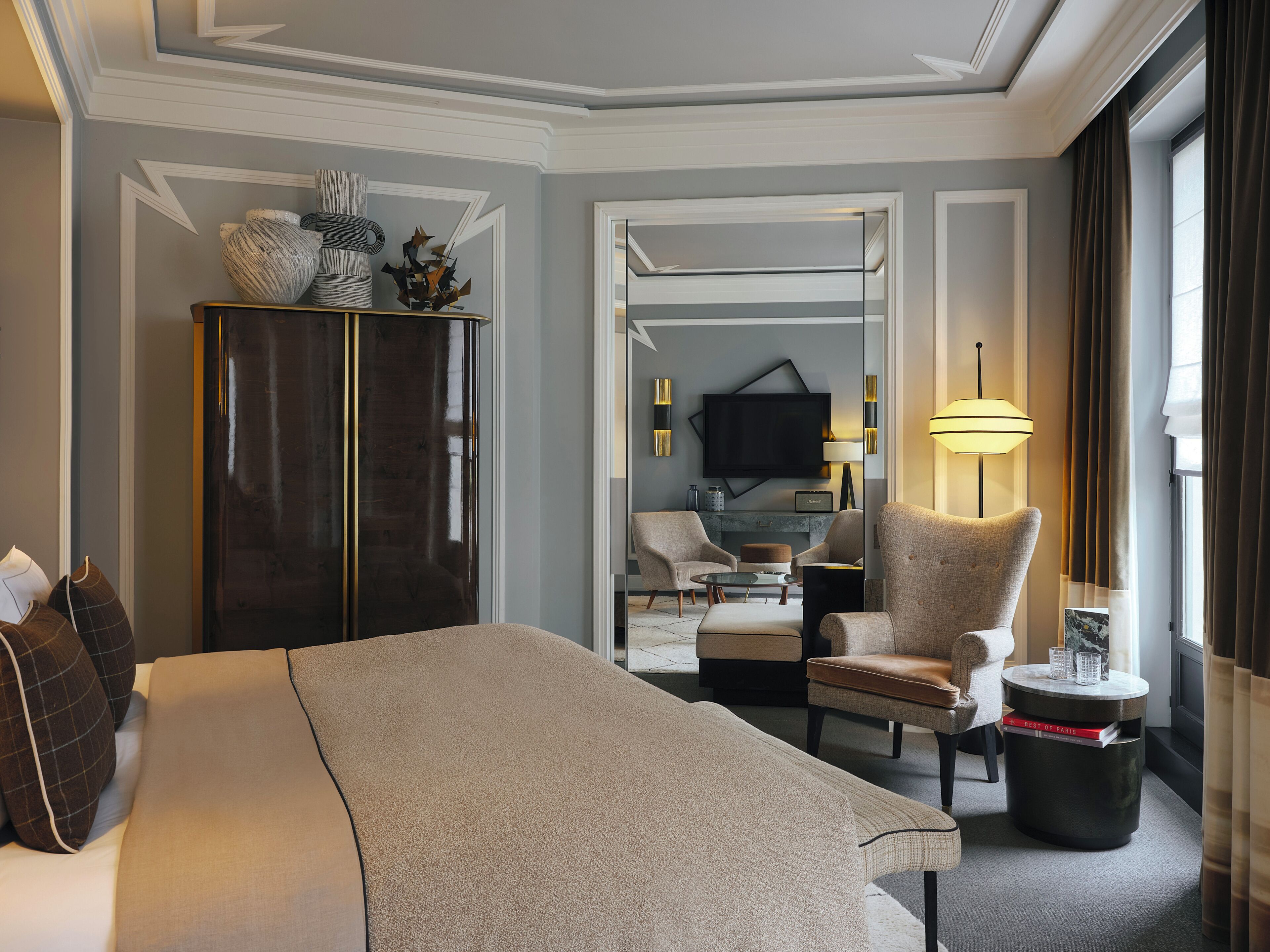 A hotel room with a bed, a chair, a small table, a lamp, and a TV.