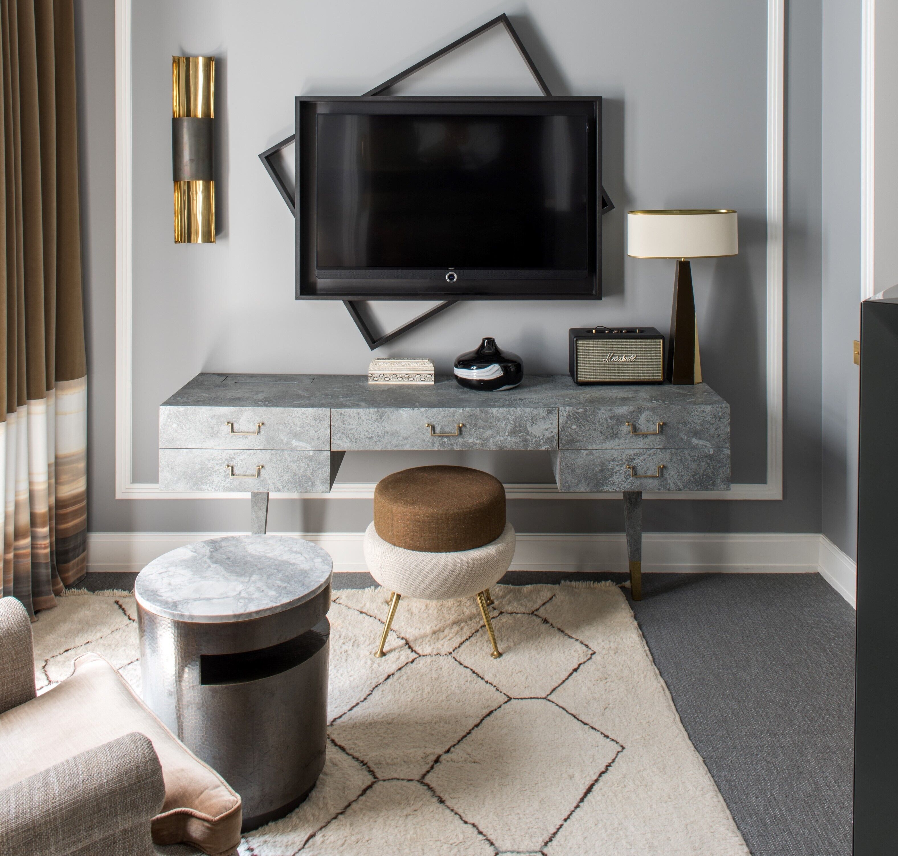 Una sala de estar moderna con un televisor de pantalla plana montado en la pared, una mesa de centro de mármol, un pouf redondo y una alfombra gris.