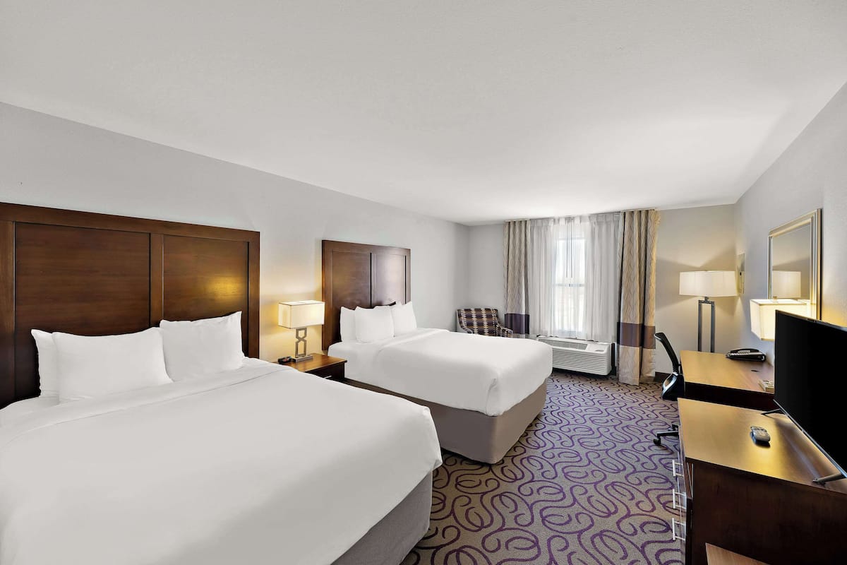 A hotel room with two beds, a desk, a TV, and a window with curtains.