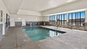 An indoor swimming pool with a clear view of the outdoors, a seating area with tables and chairs, and a modern architectural design.