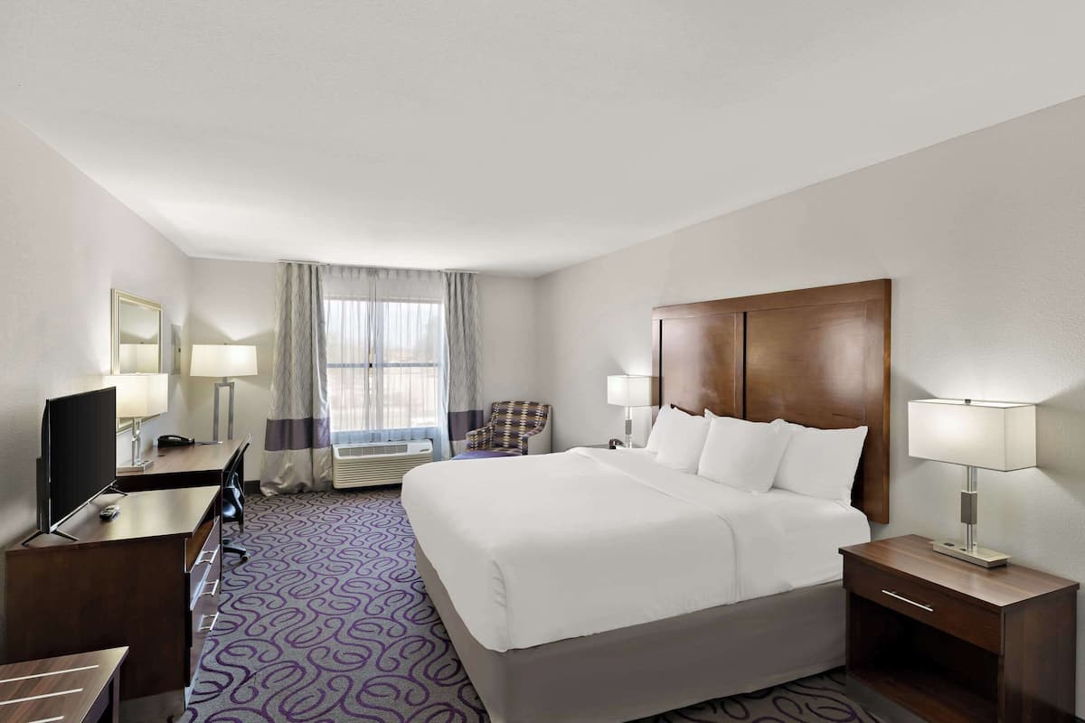 A hotel room with a large bed, a desk with a computer, a chair, a TV, and a window with curtains.