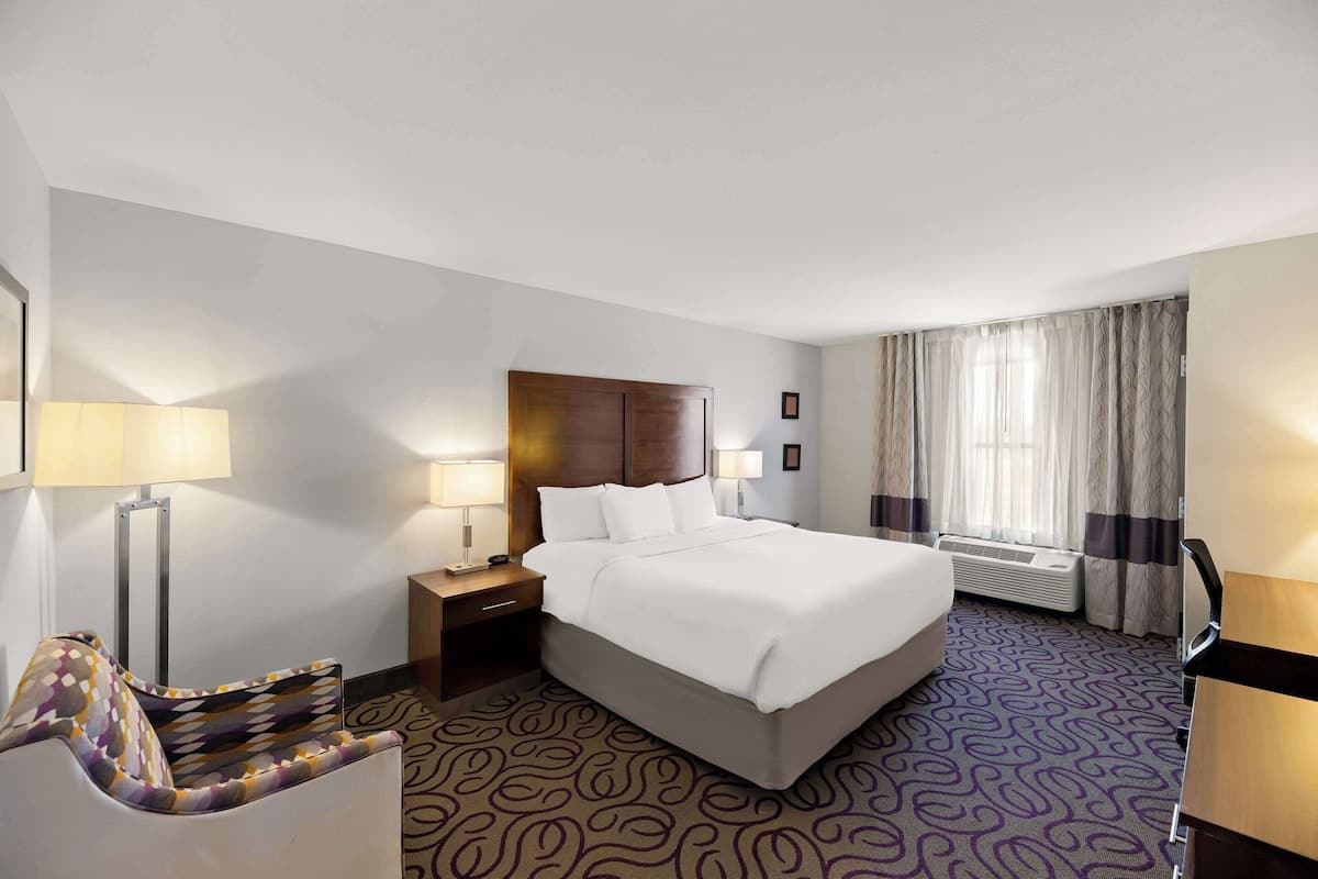 A hotel room with a large bed, bedside lamps, a desk, and a chair.