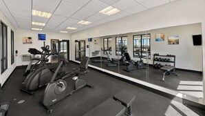 A gym with exercise equipment, a large mirror, and a view of the city through large windows.