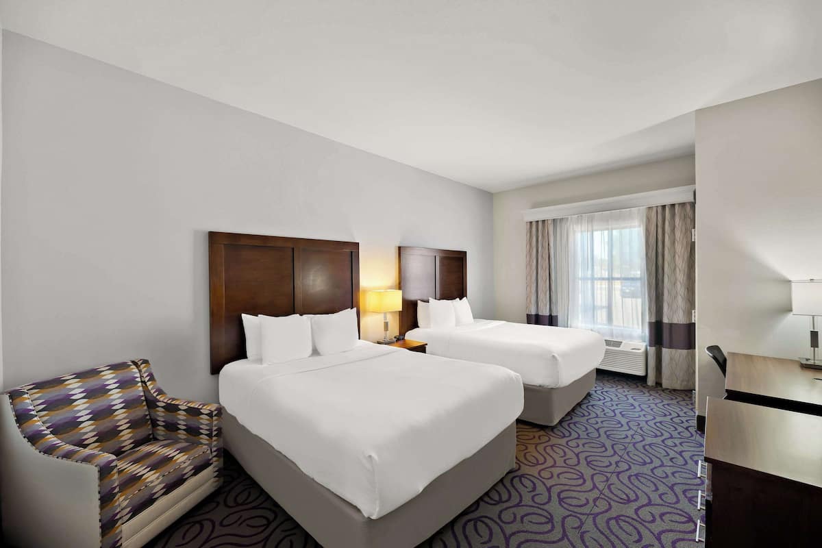 A hotel room with two beds, a sofa, a desk, and a window with curtains.